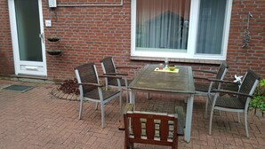 Un patio con una mesa, cuatro sillas, una puerta y un ventanal con cortinas.