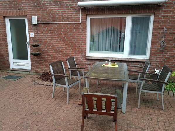 Une terrasse avec une table et quatre chaises, une porte et une fenêtre avec des rideaux.