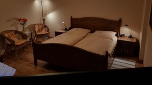 Un dormitorio con una cama de madera, dos mesitas de noche, una lámpara de pie, una silla y una pequeña mesa con un jarrón de flores.