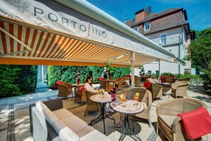 Un espace extérieur aménagé en terrasse, avec des meubles en osier, un coin salon abrité et une enseigne indiquant « PORTOFINO ».