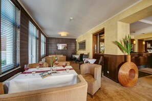 Een hotel lobby met een receptiebalie, een zithoek en grote ramen met zonwering.