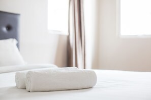 A neatly made bed with two rolled white towels and a white pillow. - Moment Hotel (Petaling Jaya)