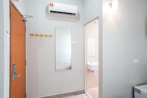 A bathroom with a wooden door, a wall-mounted air conditioner, a mirror, and a sink. - Moment Hotel (Petaling Jaya)