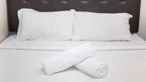 A neatly made bed with white linens and pillows, a rolled white towel on the bed, and a dark headboard. - Moment Hotel (Petaling Jaya)