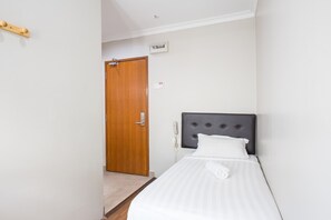 A hotel room with a wooden door, a bed with a grey headboard, and a white wall with a thermostat. - Moment Hotel (Petaling Jaya)