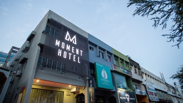A hotel with a prominent 'Moment Hotel' sign, a restaurant named 'Restoran Sandalo', and various other businesses on the ground floor. - Moment Hotel (Petaling Jaya)