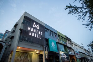 A hotel with a prominent 'Moment Hotel' sign, a restaurant named 'Restoran Sandalo', and various other businesses on the ground floor. - Moment Hotel (Petaling Jaya)