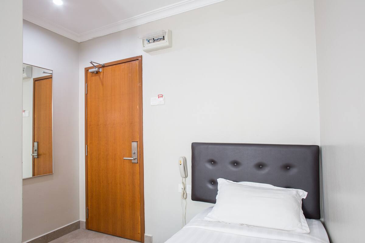 Ein Hotelzimmer mit Holztür, Nachttischtelefon und einem Bett mit weißer Bettwäsche.