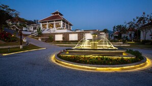 A well-lit fountain in the center of a circular driveway, surrounded by flower beds and a building with a traditional architectural style. - Le Grand Pakbeng Resort (Pakbeng)