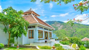 A traditional house with a tiled roof, surrounded by lush greenery and a mountainous backdrop. - Le Grand Pakbeng Resort (Pakbeng)
