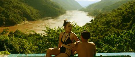 A couple sitting by a pool with a river view.