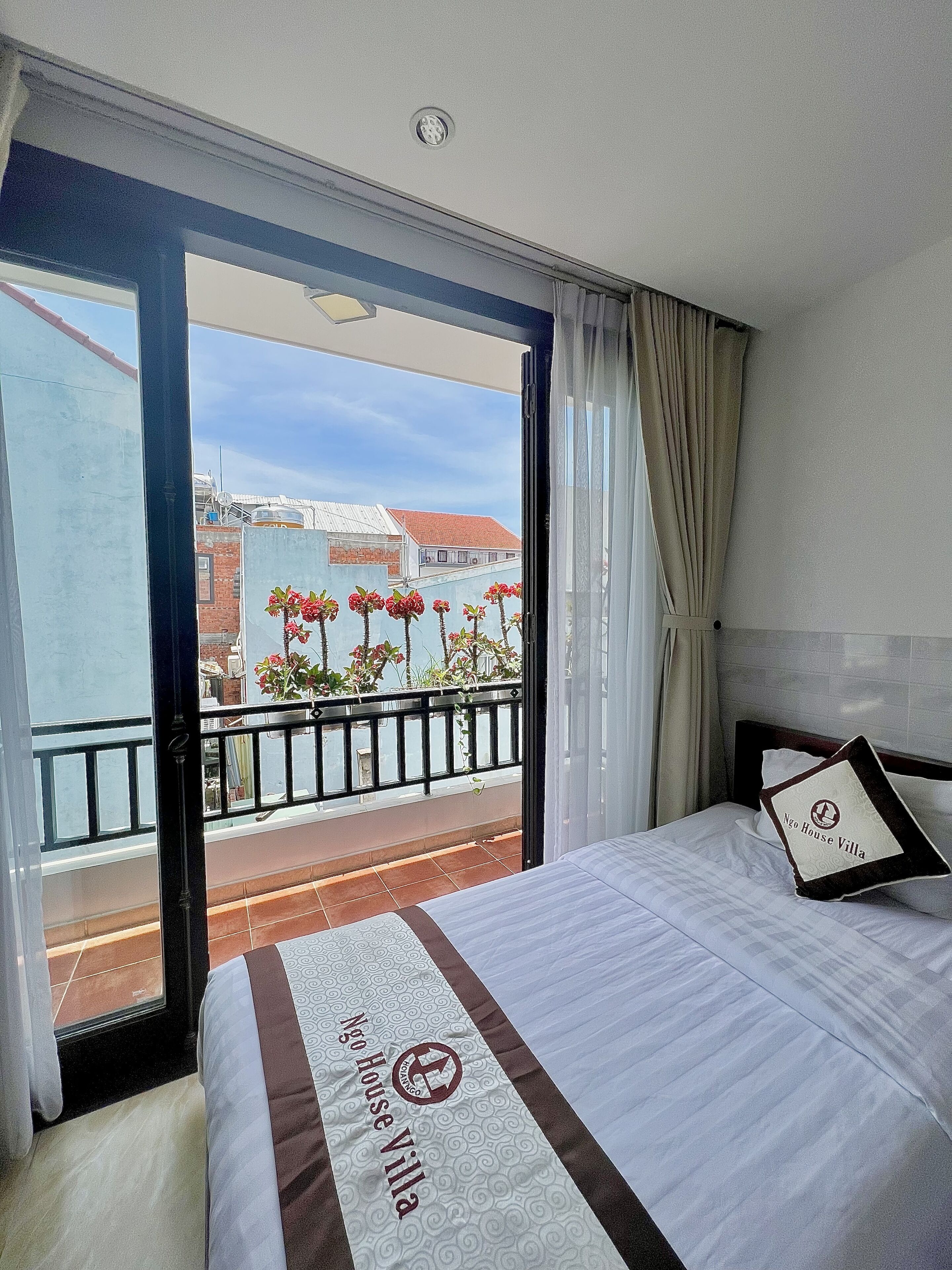 Habitación de hotel con cama, vistas a la ciudad y balcón con plantas.