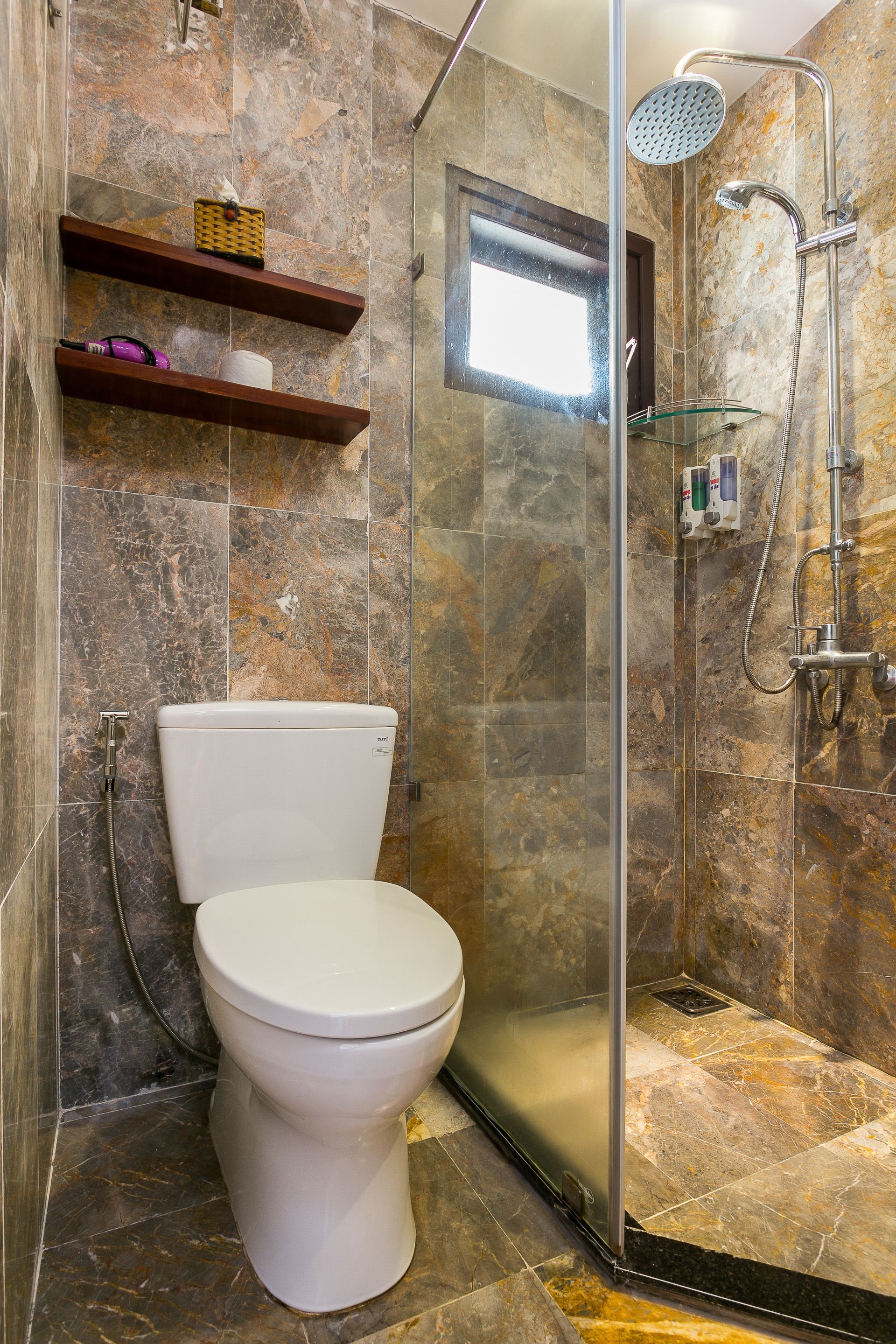 A modern bathroom with a glass-enclosed shower, a toilet, and marble walls.