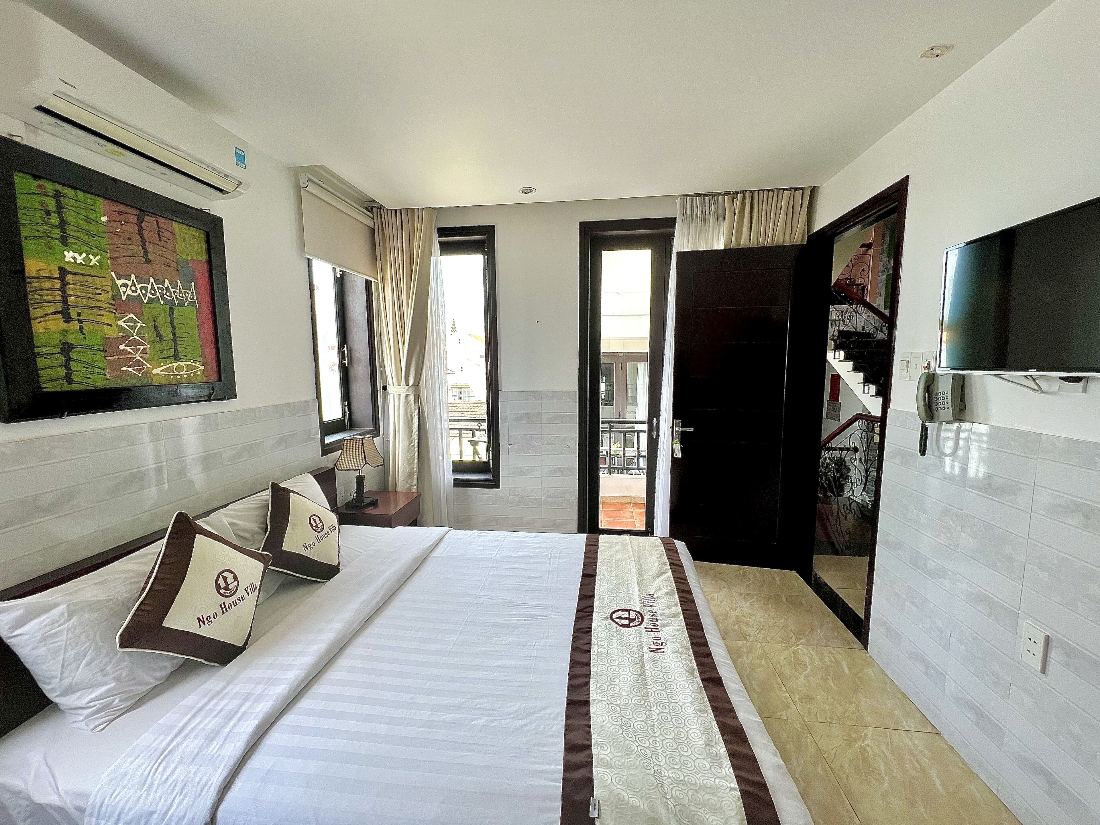 A hotel room with a large bed, a TV mounted on the wall, and a balcony visible through an open door.