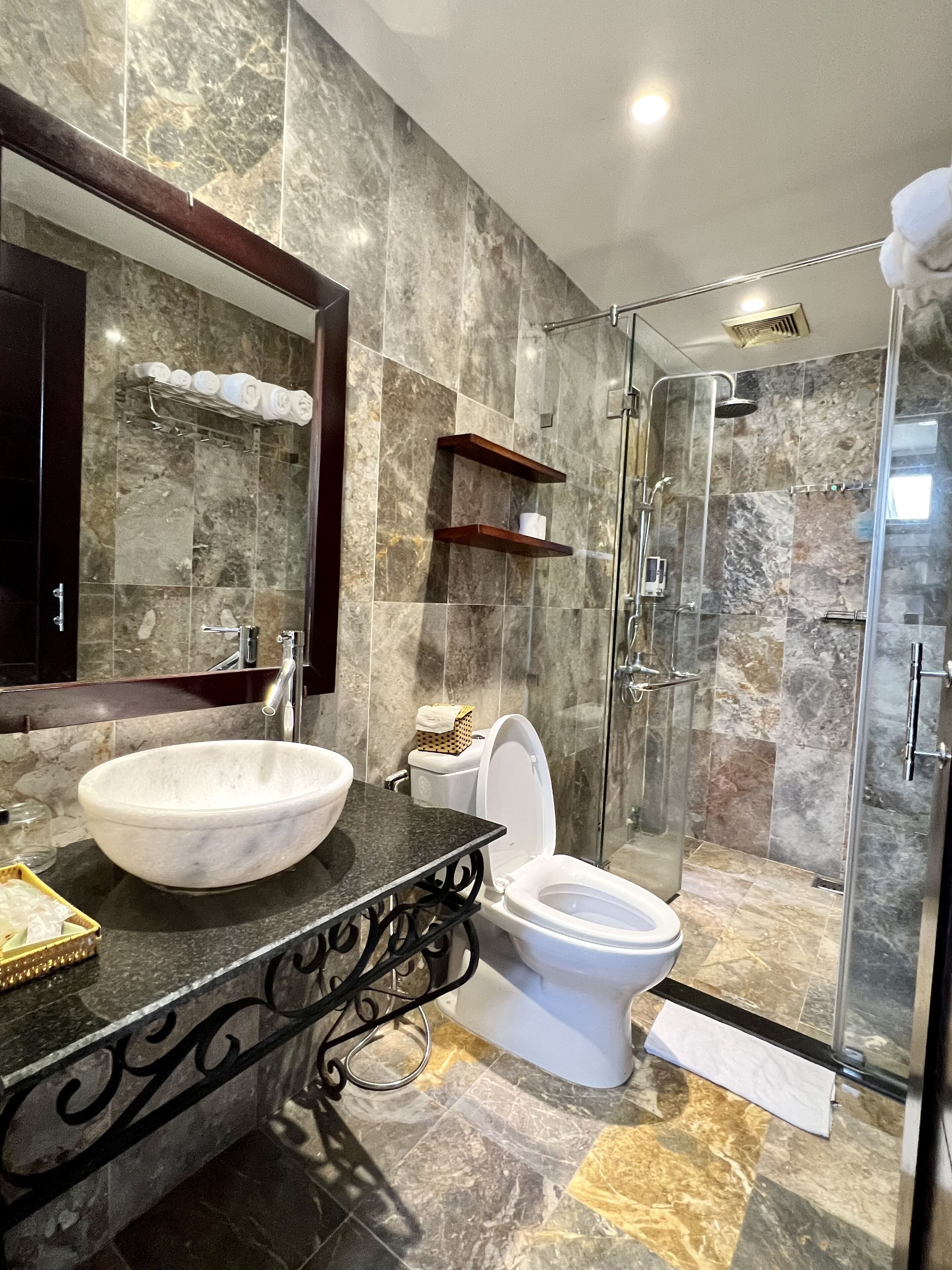 A bathroom with a marble sink, a toilet, a glass-enclosed shower, and a mirror with a towel rack.