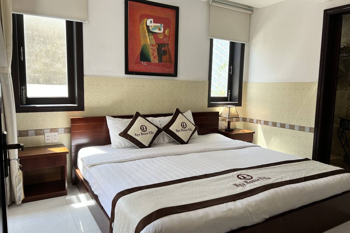 A hotel room with a bed, a nightstand, a lamp, and a window with a view.