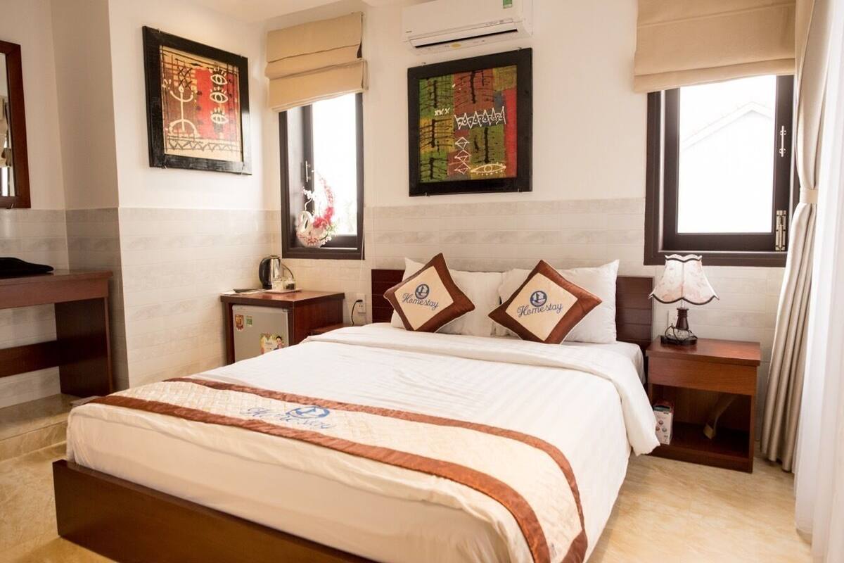 A hotel room with a bed, bedside tables, a nightstand, wall art, and a window.