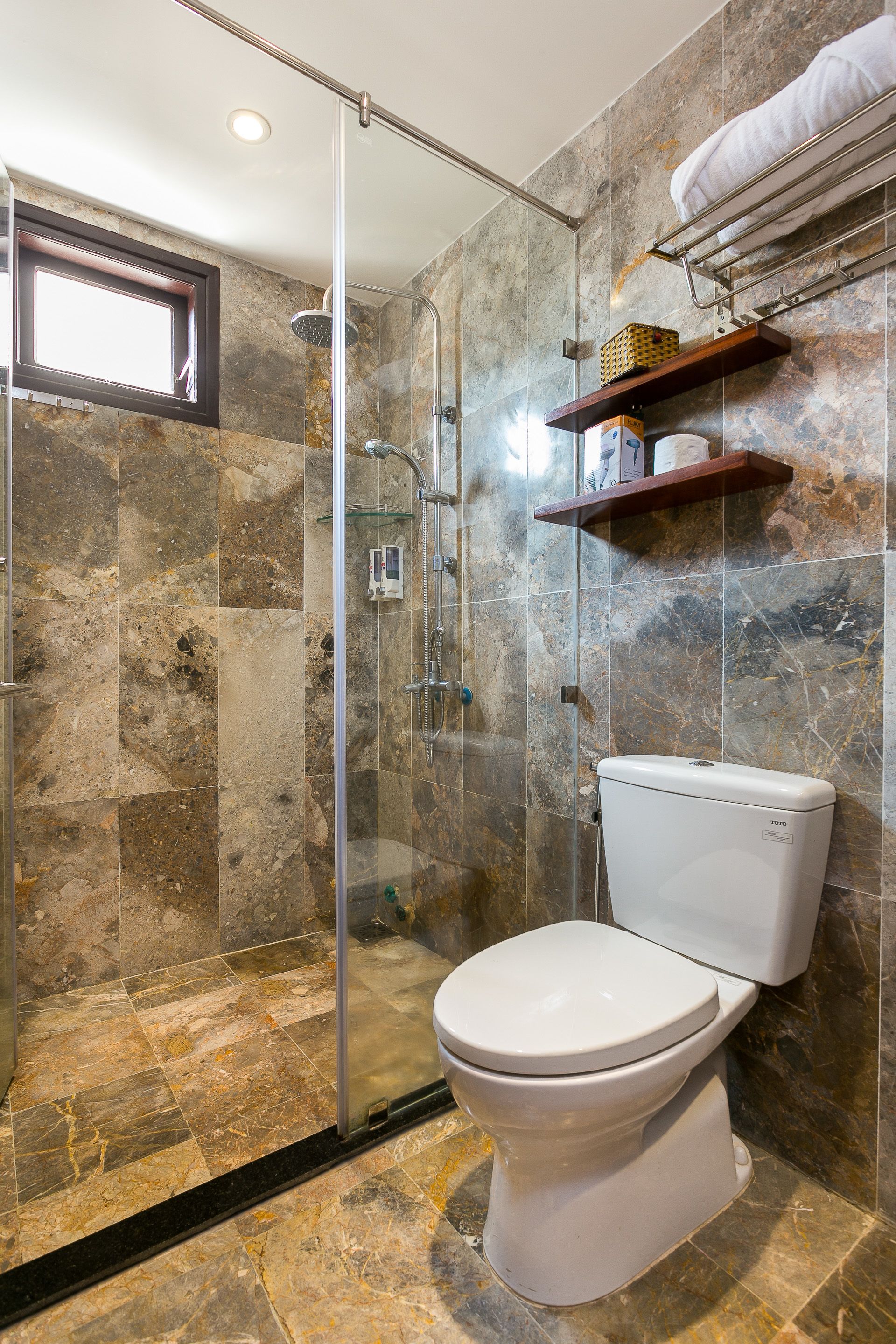 A bathroom with a glass-enclosed shower, a toilet, and a shelf with toiletries.