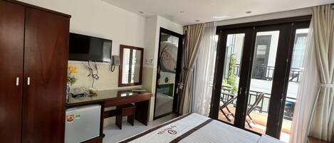 Habitación de hotel con cama, escritorio, armario, televisor y balcón con cortinas.