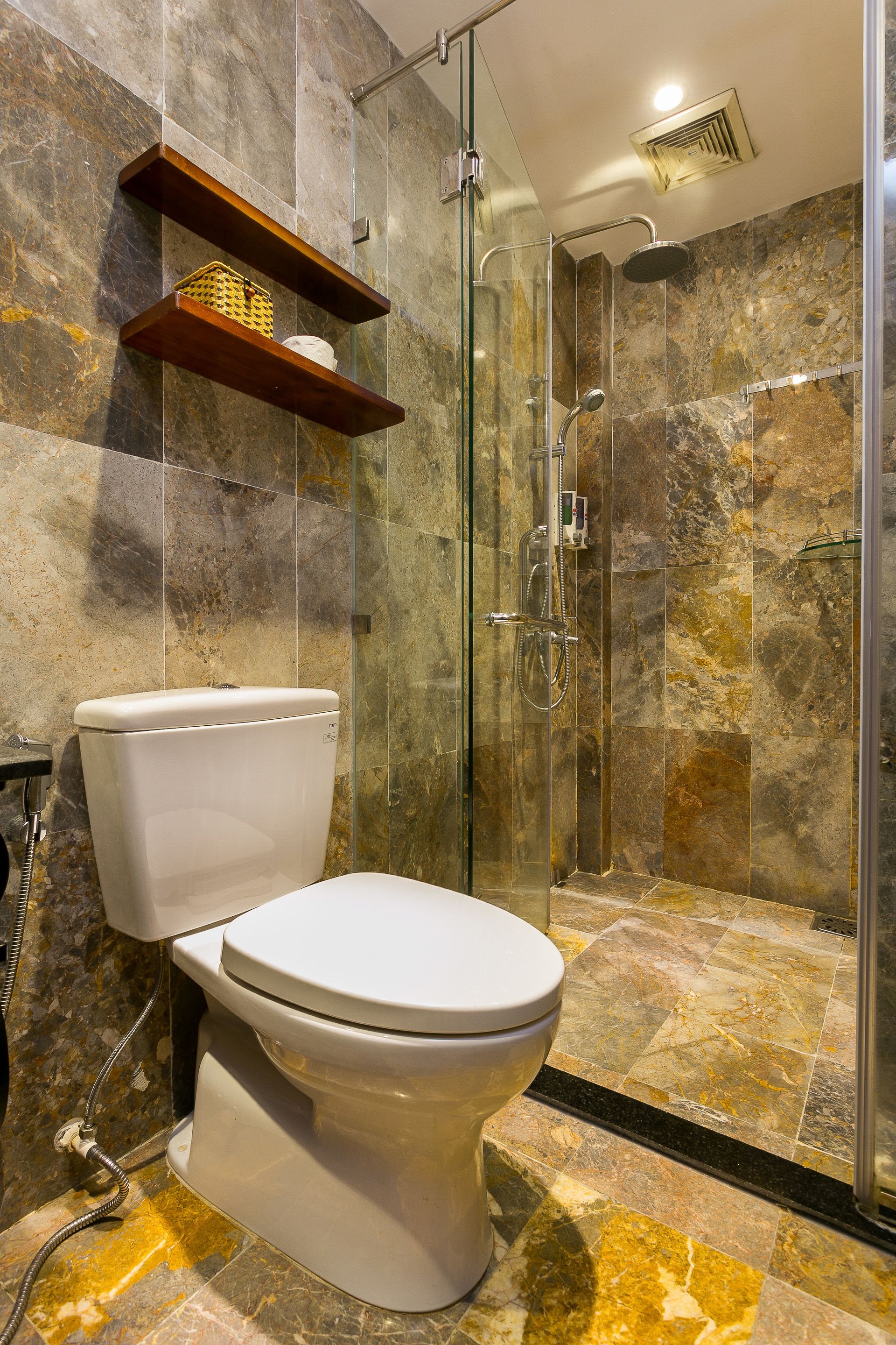 Un baño con inodoro, ducha y paredes de mármol.