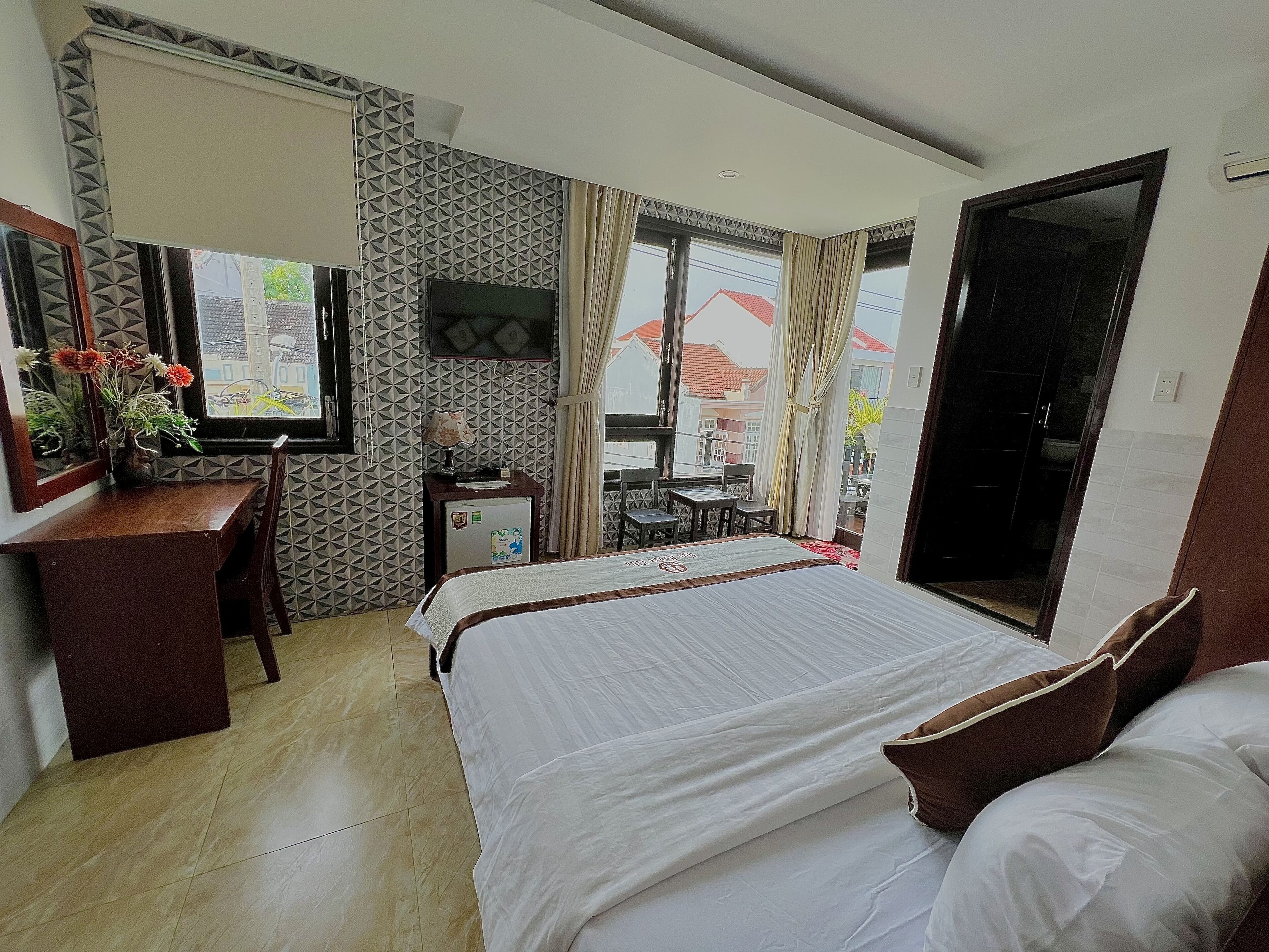 Habitación de hotel con cama, escritorio con espejo, refrigerador pequeño y ventana con cortinas.