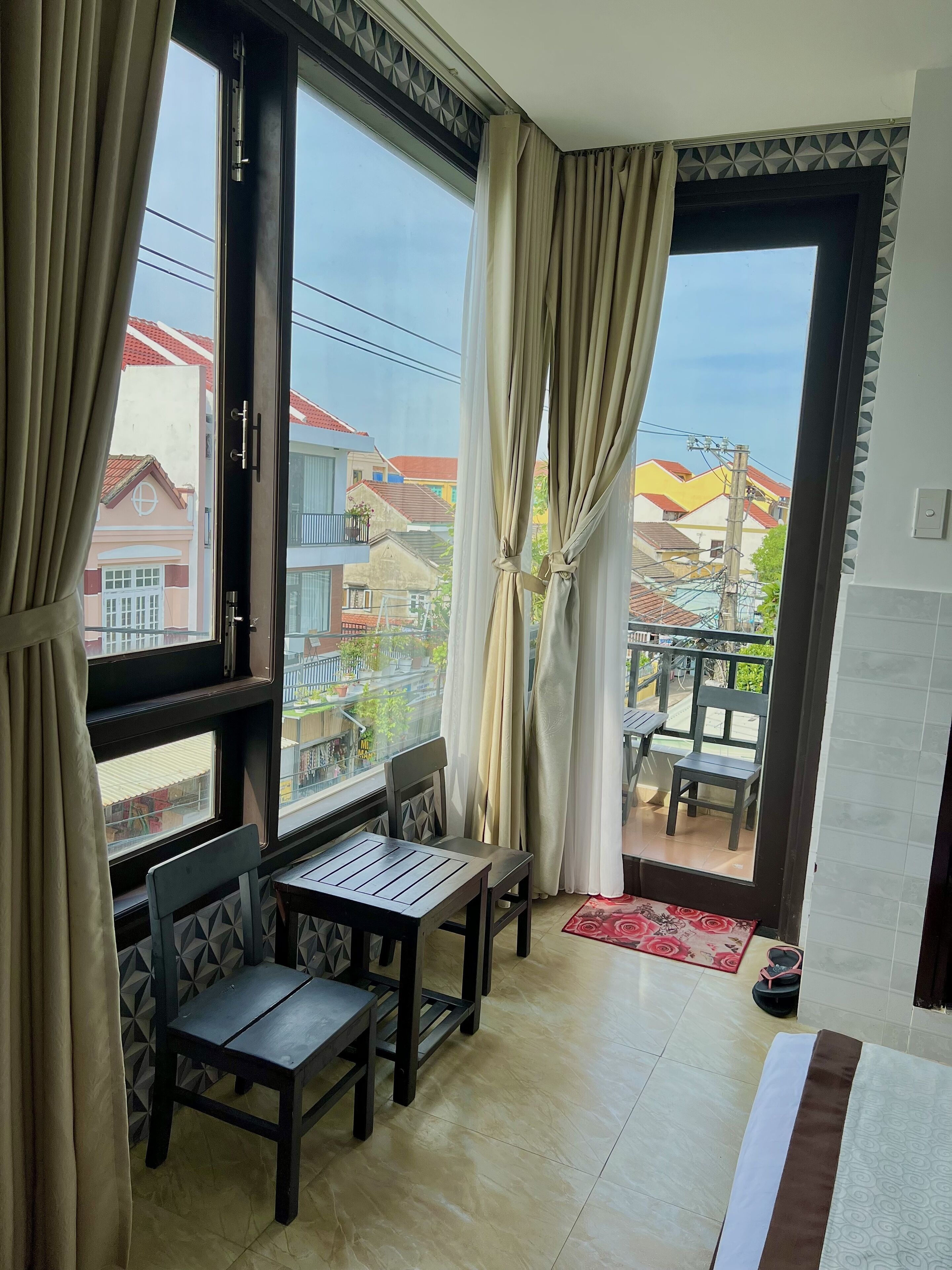 A balcony with a table and chairs, a view of neighboring buildings, and a tiled floor.