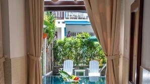 A corner room with a view of a swimming pool, two wooden chairs, a small table, and a potted plant. - Ngo Homestay (Da Nang)