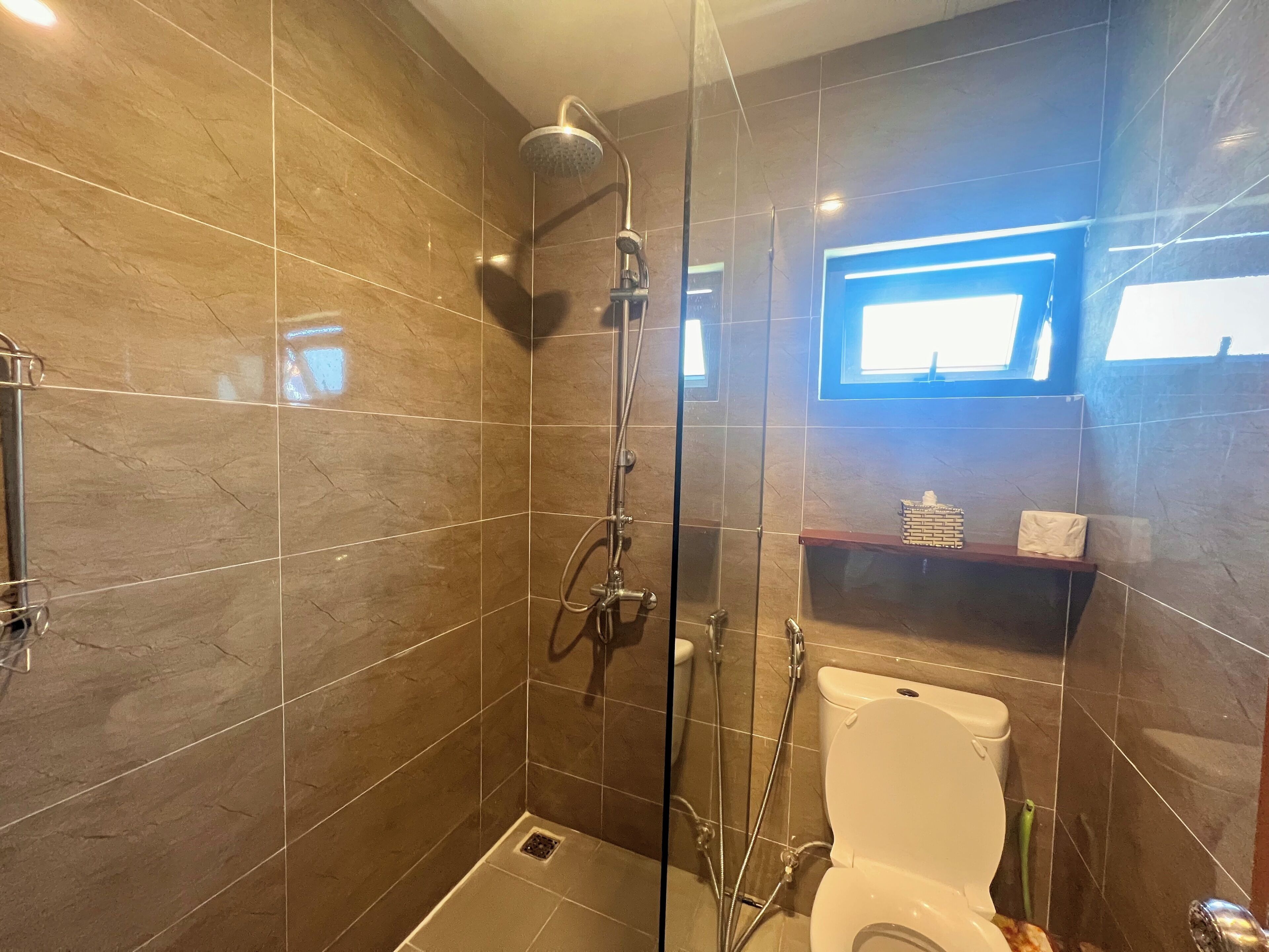 Un baño moderno con ducha de vidrio, inodoro y un estante pequeño con artículos de tocador.