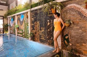 A woman in a yellow swimsuit standing by an indoor pool with a decorative wall featuring plants and stones. - Ngo Homestay (Da Nang)