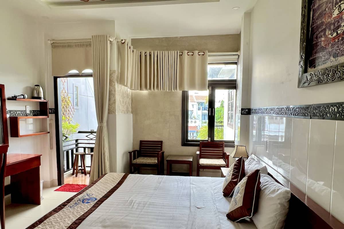 A hotel room with a large bed, two chairs, a desk, and a window with curtains.