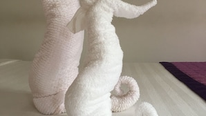 Two plush toys, one pink and one white, placed on a bed with a white sheet and a purple blanket. - Pink House Homestay (Da Nang)