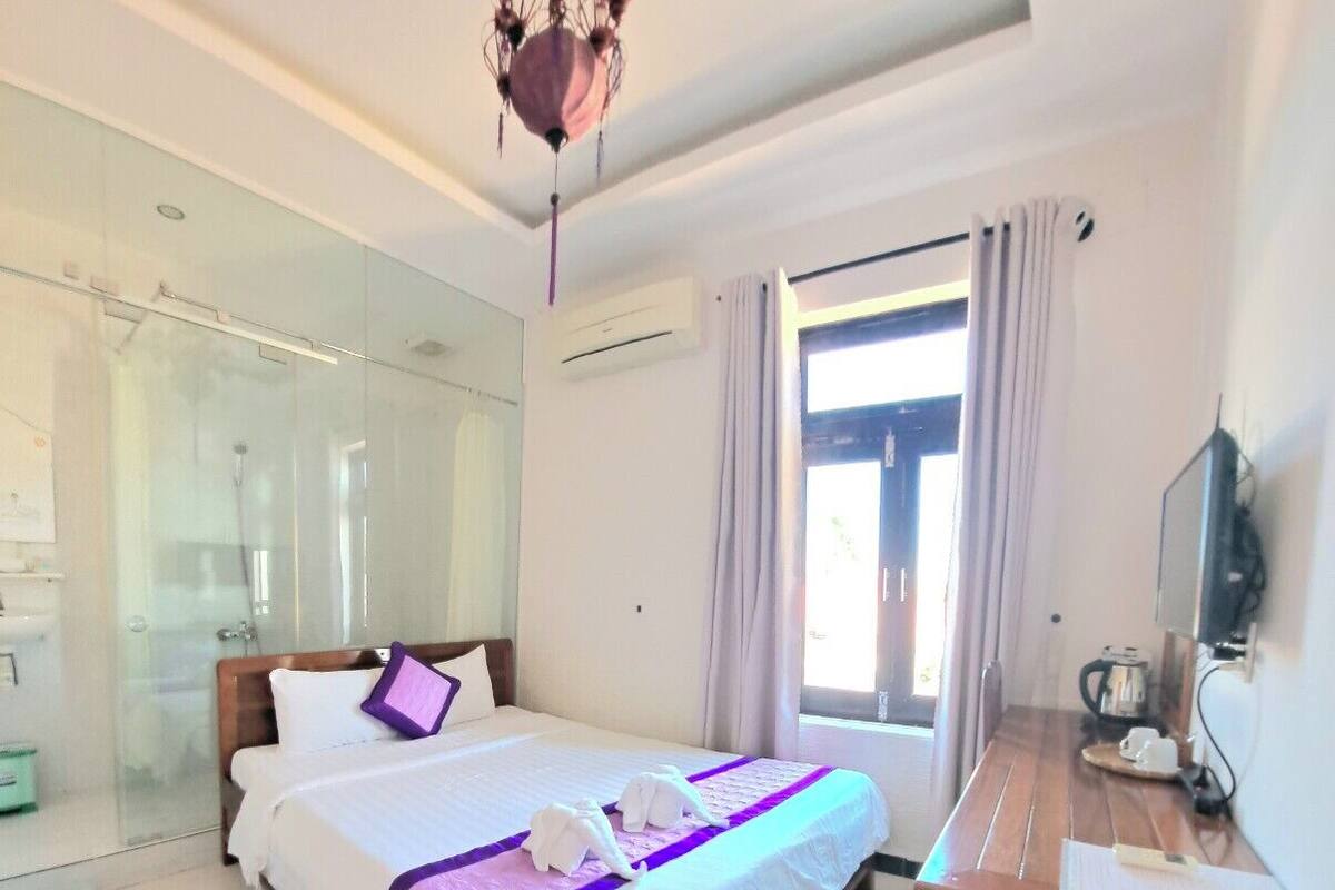 A hotel room with a bed, a desk, a television, and a glass shower enclosure.