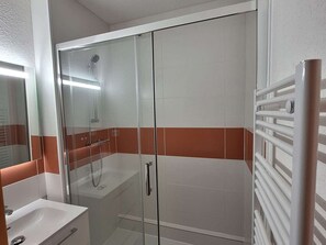 A bathroom with a glass-enclosed shower, a white sink, and a towel rack.