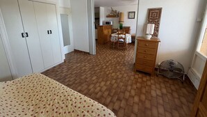 A bedroom with a bed, wardrobe, and a dining area with a table and chairs. - Spacious 3-bedroom apt with terrace, pool and parking near the beach (Port Barcarès)