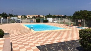 A swimming pool with a checkered floor, surrounded by a fence, and a clear sky in the background. - Spacious 3-bedroom apt with terrace, pool and parking near the beach (Port Barcarès)