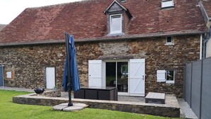 Ein Steinhaus mit rotem Ziegeldach, einer überdachten Terrasse mit Gartenmöbeln und einem Rasengrundstück.
