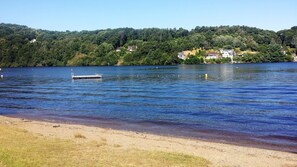 Un lago con un muelle, una playa de arena y casas al fondo.