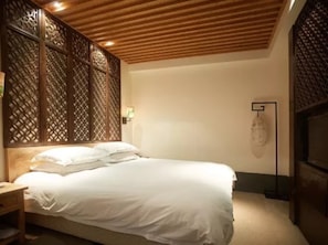 A bedroom with a wooden slatted headboard, a bed with white bedding, a bedside table, and a wall-mounted light fixture.