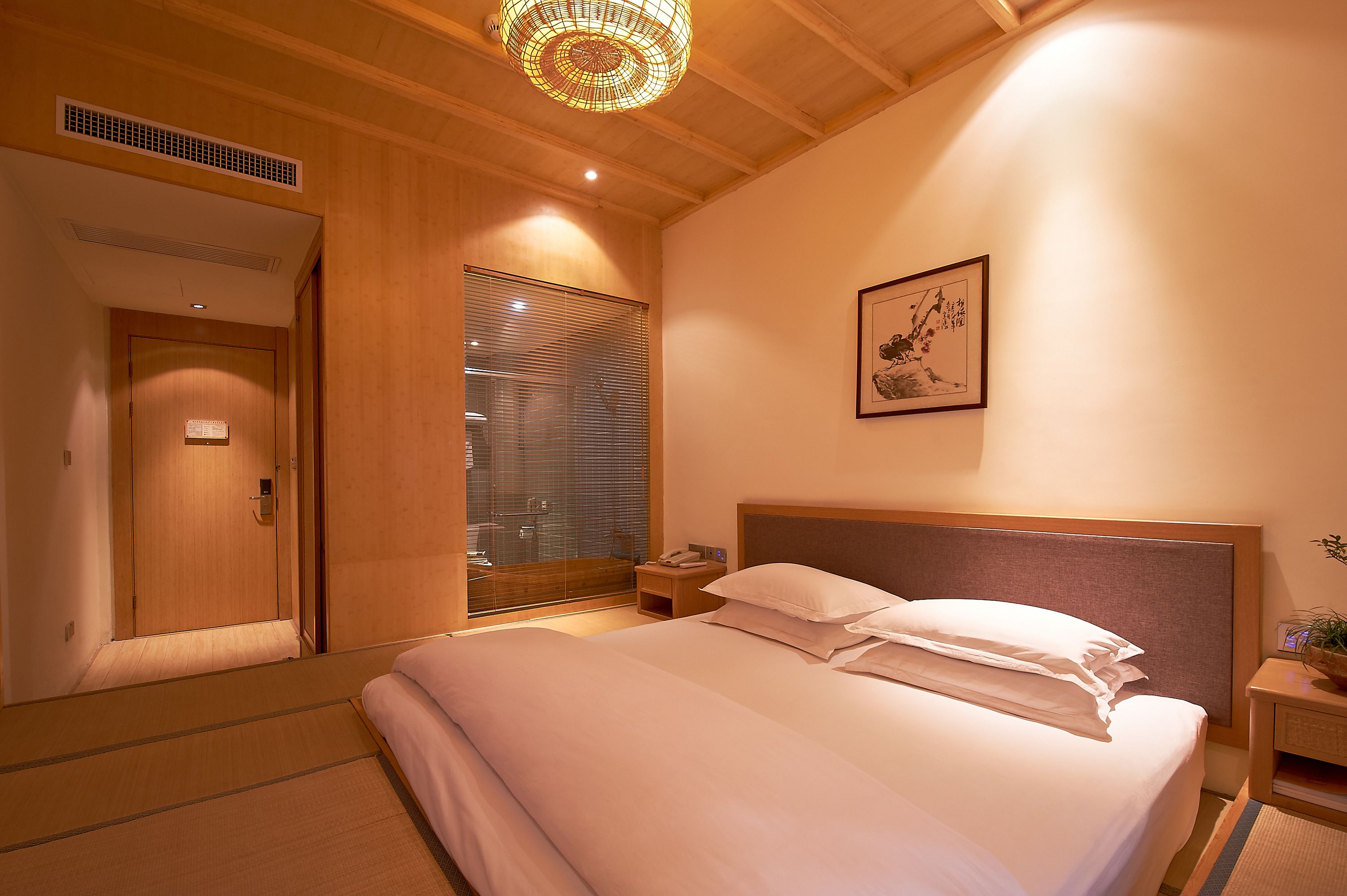 Habitació d'hotel amb sostre de fusta, llit amb roba de llit blanca, tauleta de nit amb una làmpada i una obra d'art emmarcada a la paret.