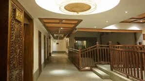 A hallway with a wooden door on the left, a staircase with a wooden railing, and a circular ceiling light fixture. - Xiangji Yinyu Boutique Hotel - Hangzhou (Hangzhou)
