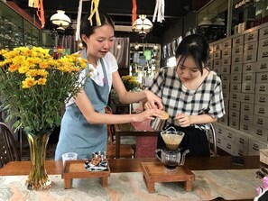 A restaurant interior with a wooden table, a vase of yellow flowers, and a coffee station. - Jaritt Nymmanh (Chiang Mai)
