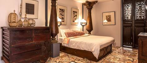 Un dormitorio con una cama grande, muebles de madera, baldosas de suelo estampadas y obras de arte en las paredes.