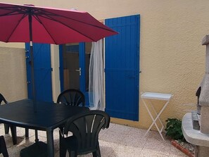 Eine Terrasse im Freien mit Tisch und Stühlen, einem roten Sonnenschirm und einer blauen Tür.
