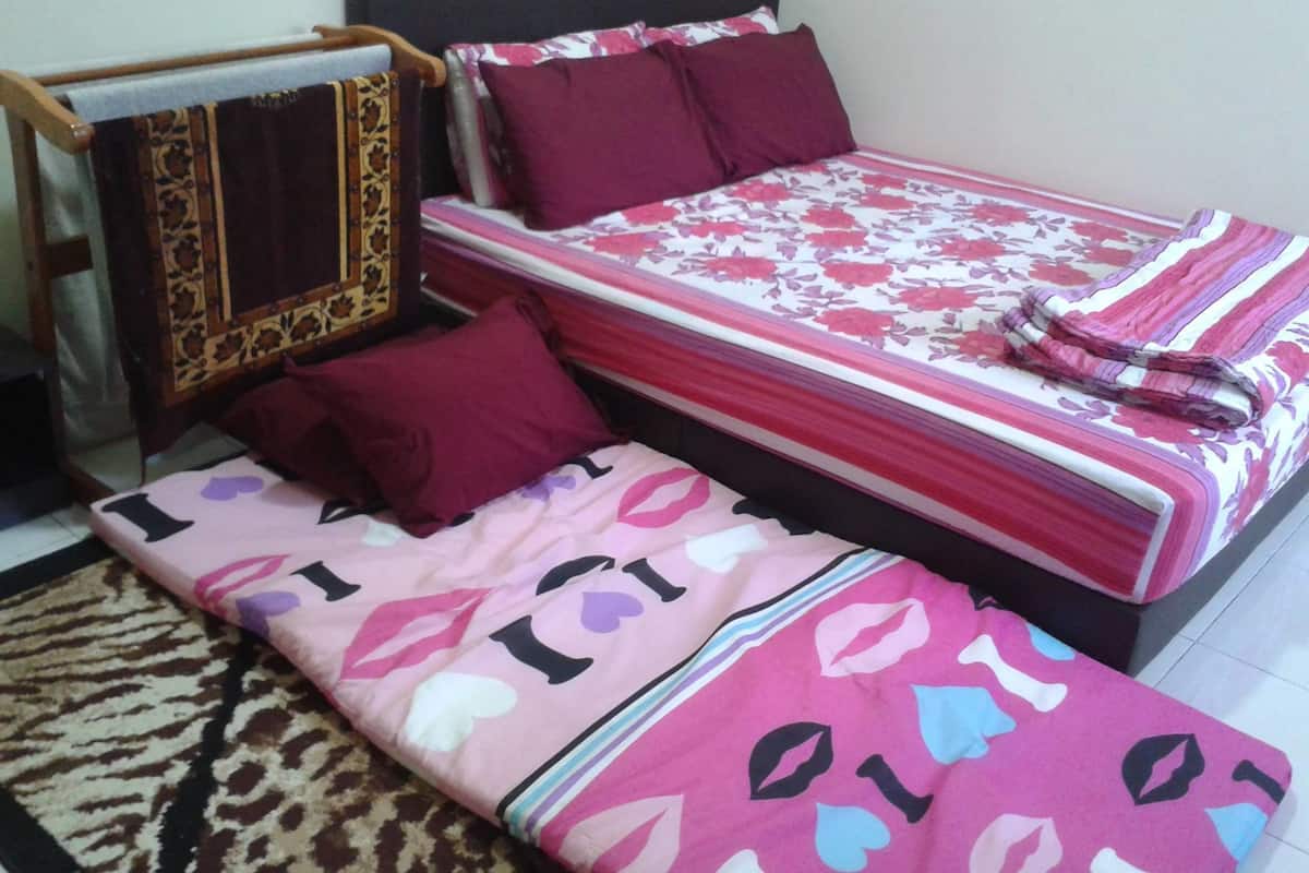 A bed with a floral bedspread and multiple pillows, a wooden headboard, and a patterned rug.