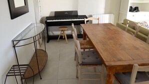 Ein Essbereich mit Holztisch und -stühlen, einem Klavier, einem Spiegel und einem Korbstuhl.