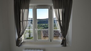 Ein Zimmer mit Fensterblick auf einen Weinberg und Hügel.