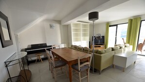 Ein geräumiges Wohnzimmer mit Klavier, Esstisch und Sofa.