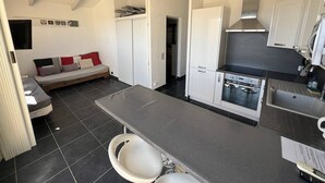 Une cuisine compacte avec un coin repas, un four encastré et un petit coin salon avec un canapé et un lit.