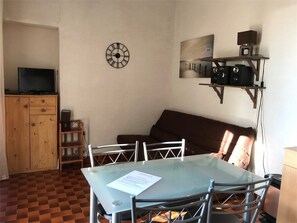 A dining area with a glass table and metal chairs, a wooden cabinet with a television, and a clock on the wall.