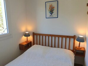 A bedroom with a wooden headboard, two bedside tables with lamps, a white textured bedspread, and a framed artwork on the wall.
